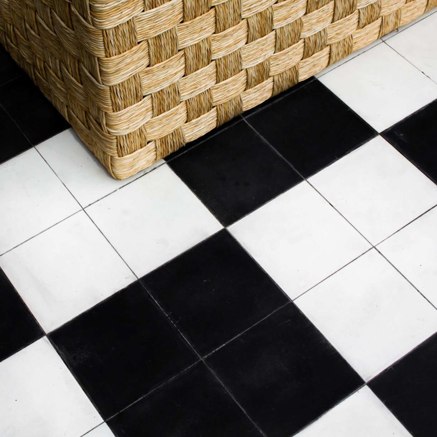 a wicker basket sitting on a black and white tiled floor.