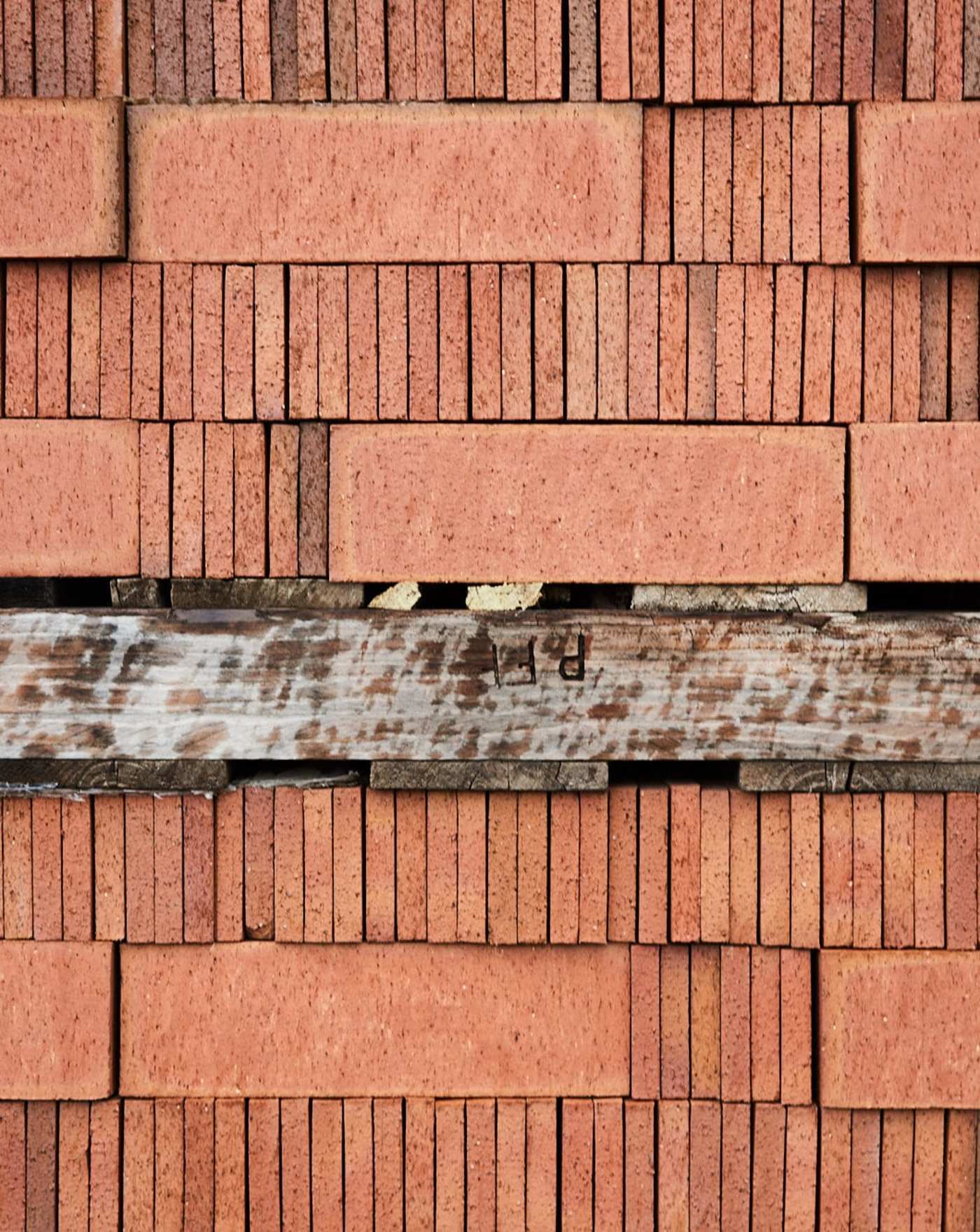 several stacks of red bricks diveded by a wooden plank.