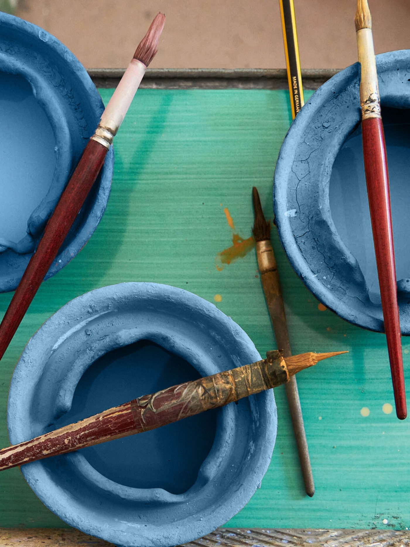 a green table with paint brushes and blue bowls on it.