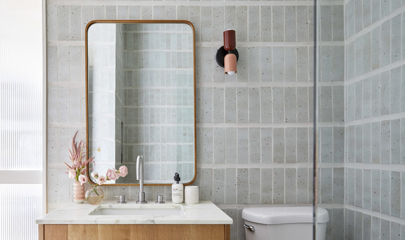 a bathroom with grey tiled walls, a sink, toilet and a mirror.