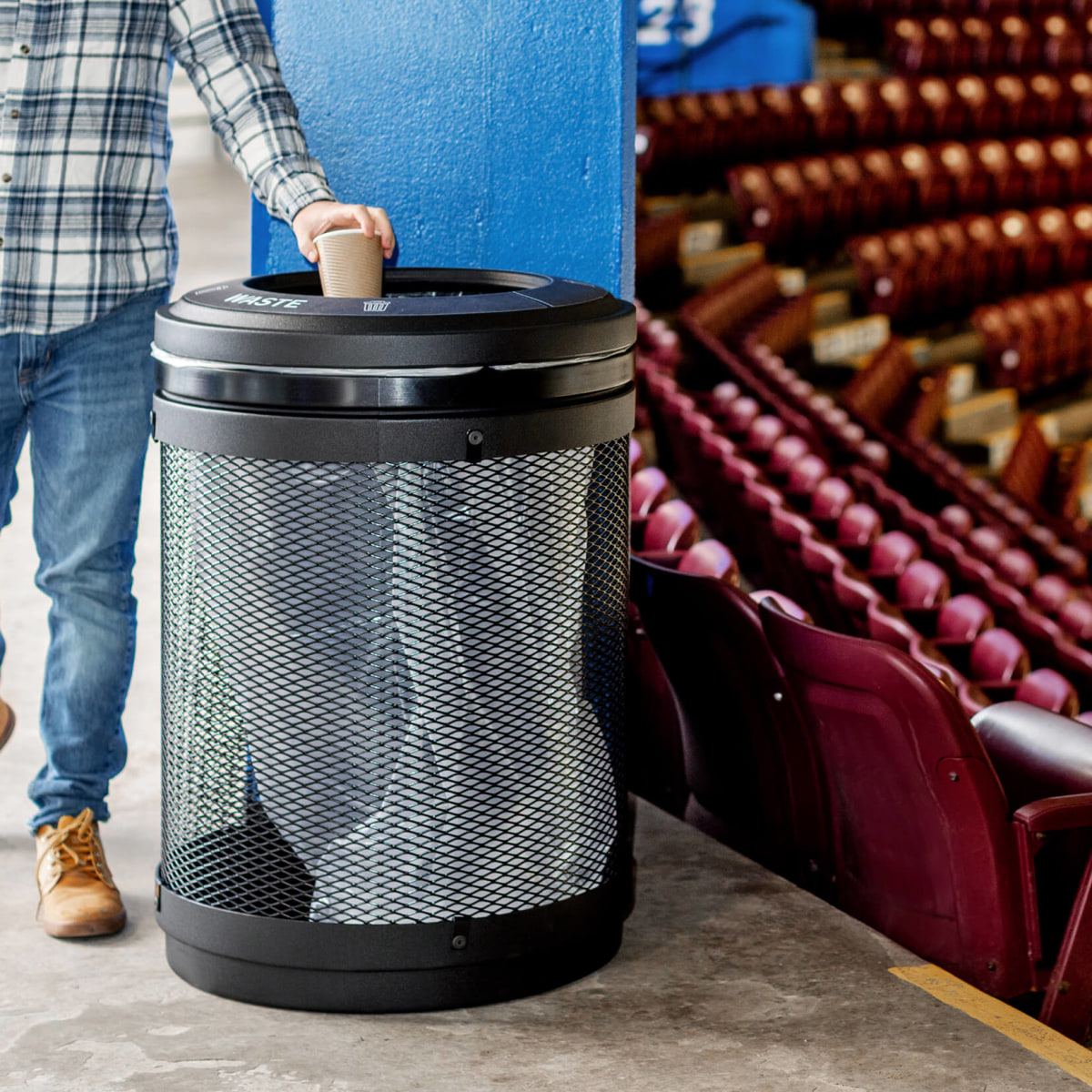 black metal and plastic waste bin indoors at a hockey rink with a person depositing waste