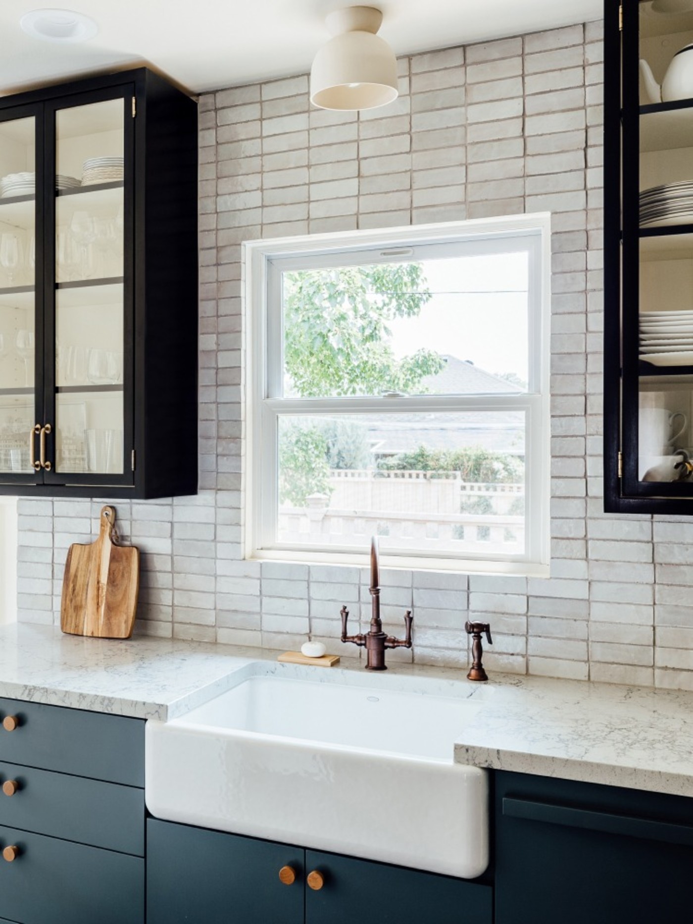 a kitchen sink with white tile backsplash, black cabinets and window.