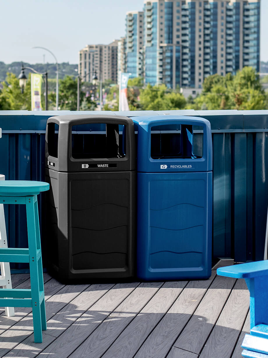 black waste bin and blue recycling bin with canopy lids made from durable 100% post-consumer recycled plastic sitting outside on a rooftop patio