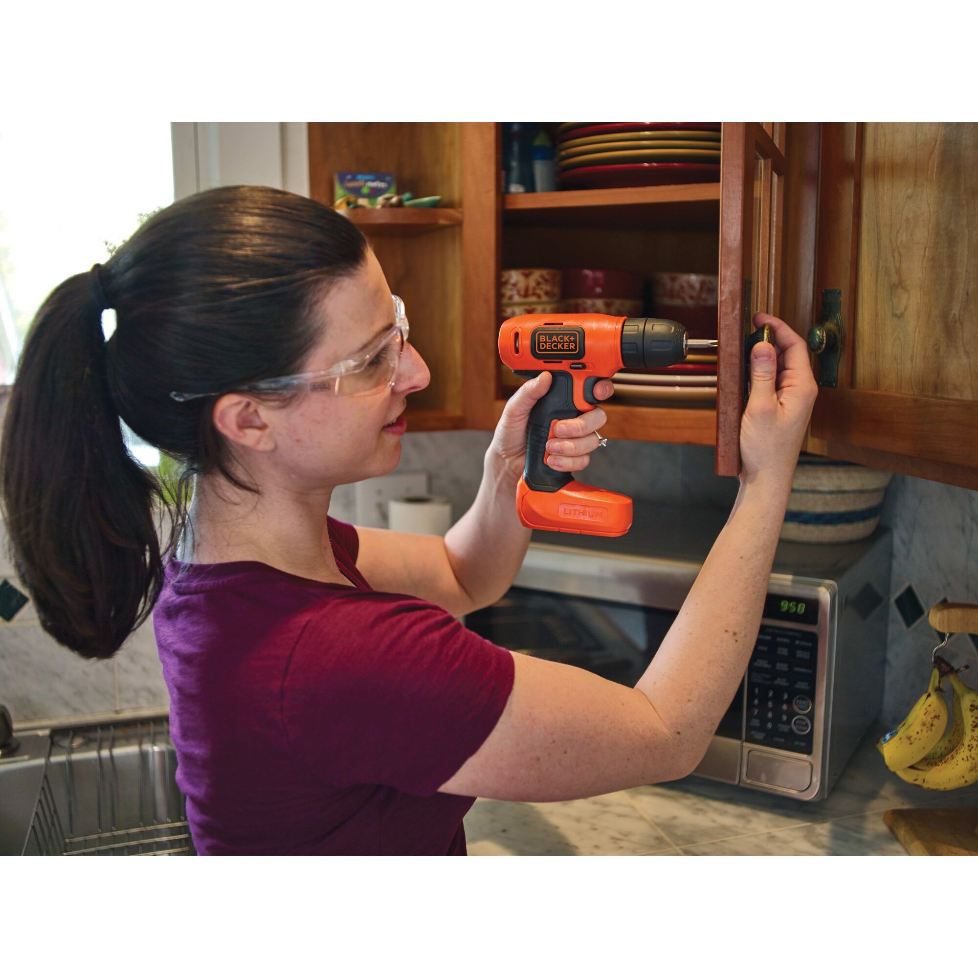 Cordless lithium drill being used attach a knob to the cabinet by a person.