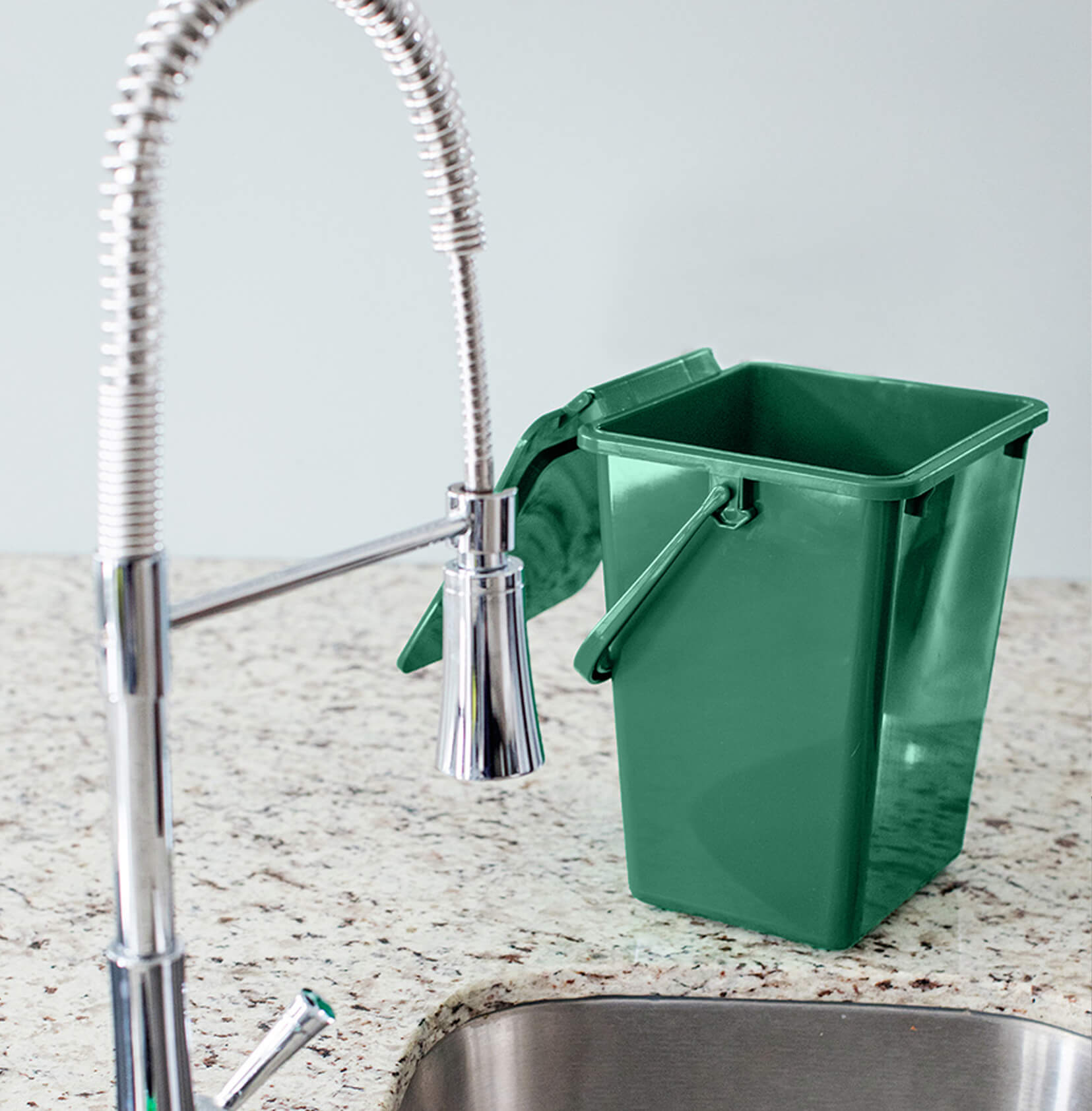 green kitchen organics collection bin sitting on a kitchen counter beside the sink with the lid open