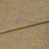 Woven curtain-like fabric with mustard-yellow leaf motif, folded once across the frame and overlapping; close-up view revealing textured taupe weave under soft, even studio lighting.