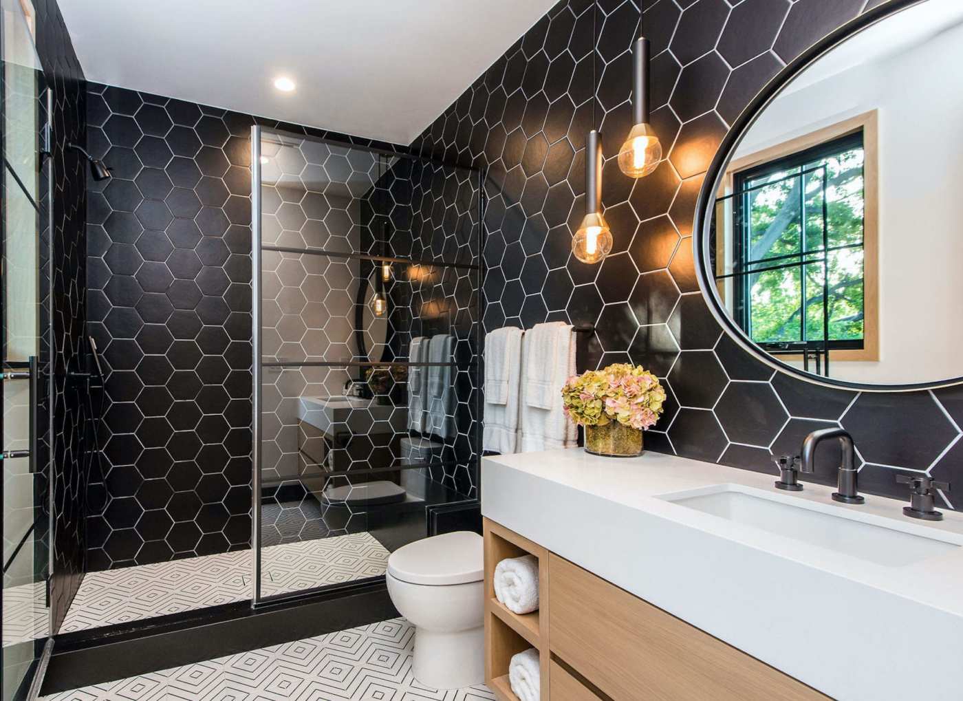 a bathroom with black hexagon tile and a round mirror.