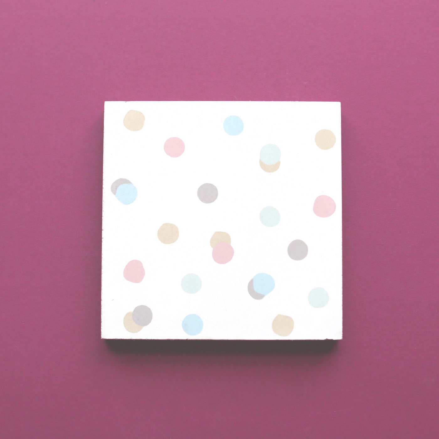 a white tile with multicolored polka dots on a pink surface.