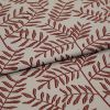 Woven beige upholstery fabric patterned with rust-red fern branches, folded and overlapped across the frame, close-up studio-lit view highlighting the woven texture and printed details.