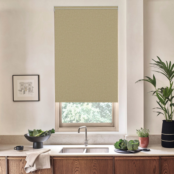 Beige roller blind hangs down over a kitchen window, blocking light; stainless faucet and double sink sit below on a marble countertop with vegetables, potted plants, and wooden cabinets around.