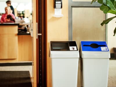 double waste and recycling containers with color-coded lids at the entrance to a college campus library