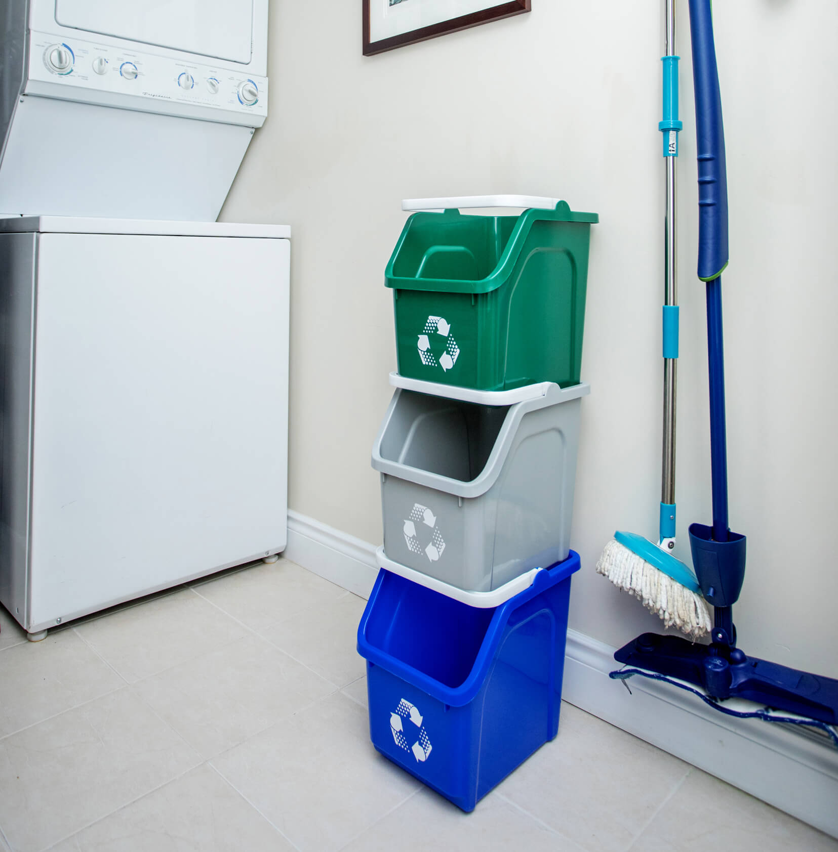 stackable plastic recycling bins in an apartment laundry room on the floor beside a washing machine