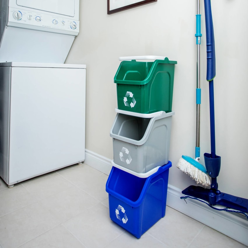 stackable plastic recycling bins in an apartment laundry room on the floor beside a washing machine