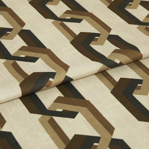 Cream fabric sample printed with repeating brown and black interlocking geometric shapes; folded across the center; close-up studio shot with soft, even lighting on a neutral background.