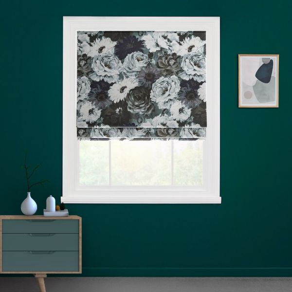 Floral Roman blind, gray-and-white blooms, lowered over the upper sash, softly filtering daylight; in a room with deep teal walls, white trim, small dresser and a framed abstract print.