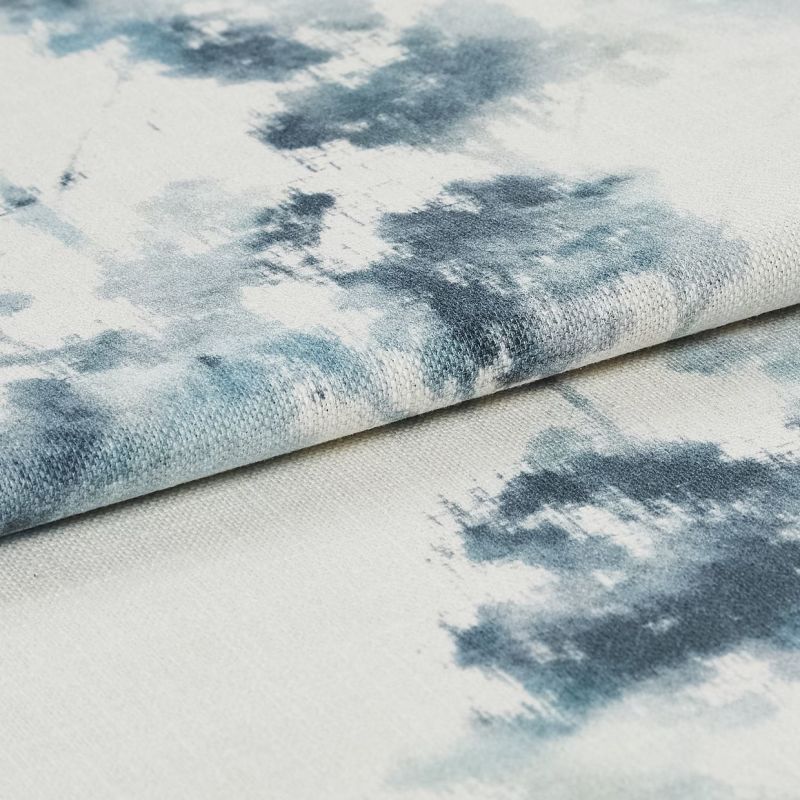 Folded woven fabric patterned with blueâ€‘gray watercolor blotches is layered in a close-up, softly lit view, revealing coarse weave texture against a muted offâ€‘white background.