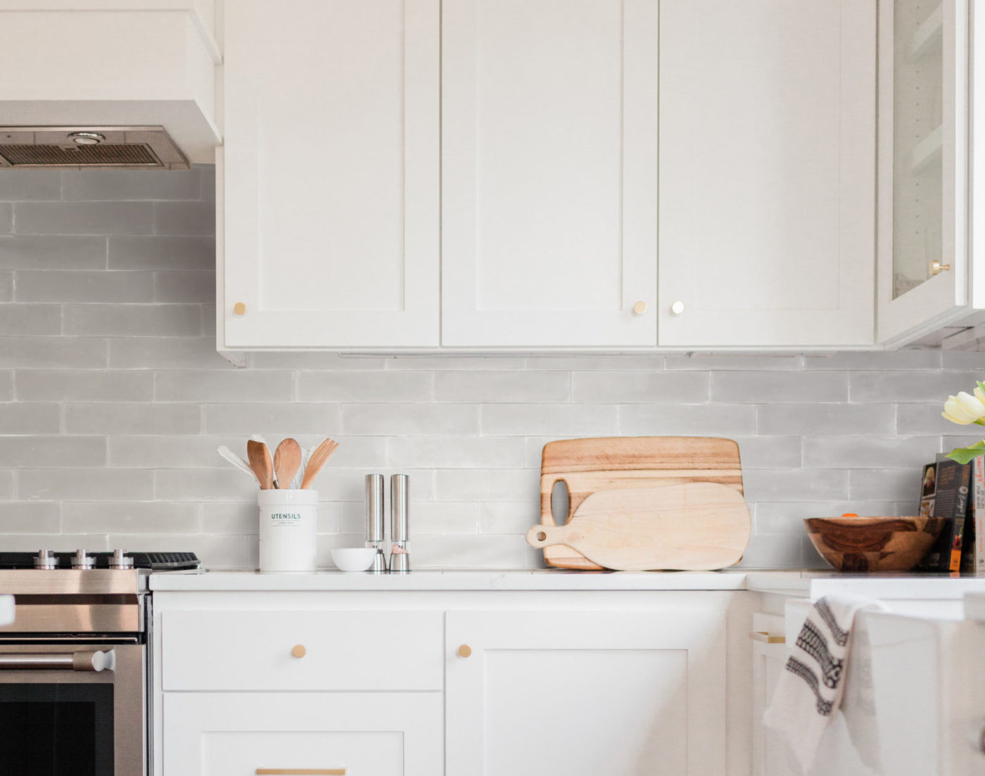 a kitchen with white cabinets, grey tile walls, and a stove.