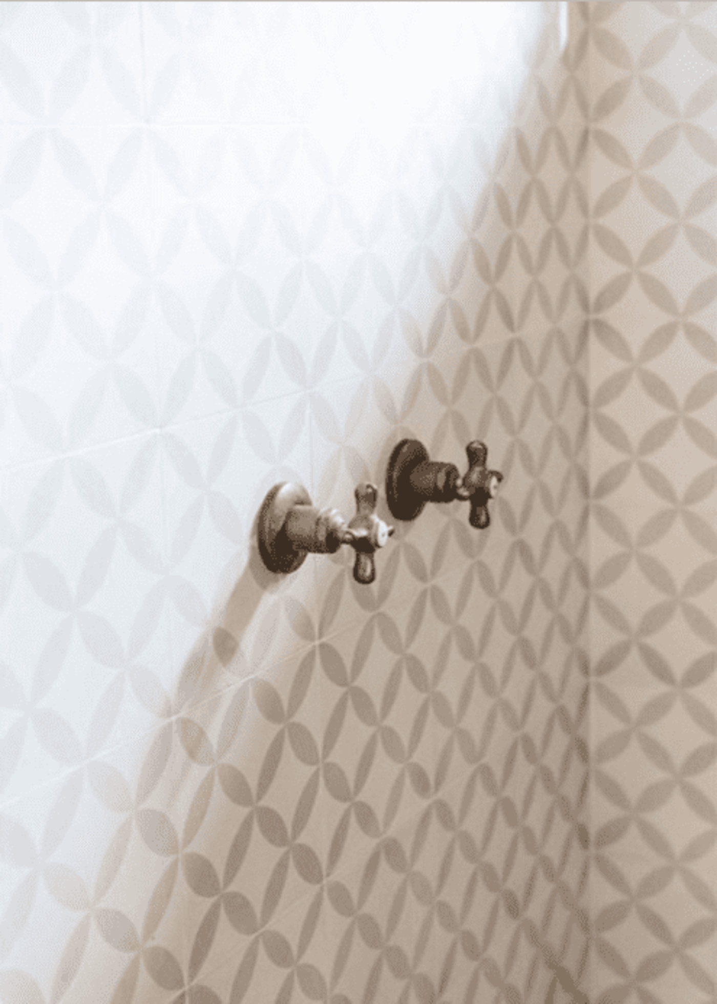 a shower with grey and white patterned tile and two knobs.