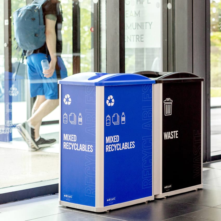 a mixed recyclables and waste station with large body signs sitting inside a recreation facility