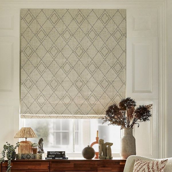 Beige fabric Roman blind with stitched diamond pattern, lowered to cover the window and softly filtering daylight. Beside a wooden console with lamp, books and a vase of dried flowers.
HOMES FOR OUR TIME
EVERYTHING ABIGAIL AHERN
