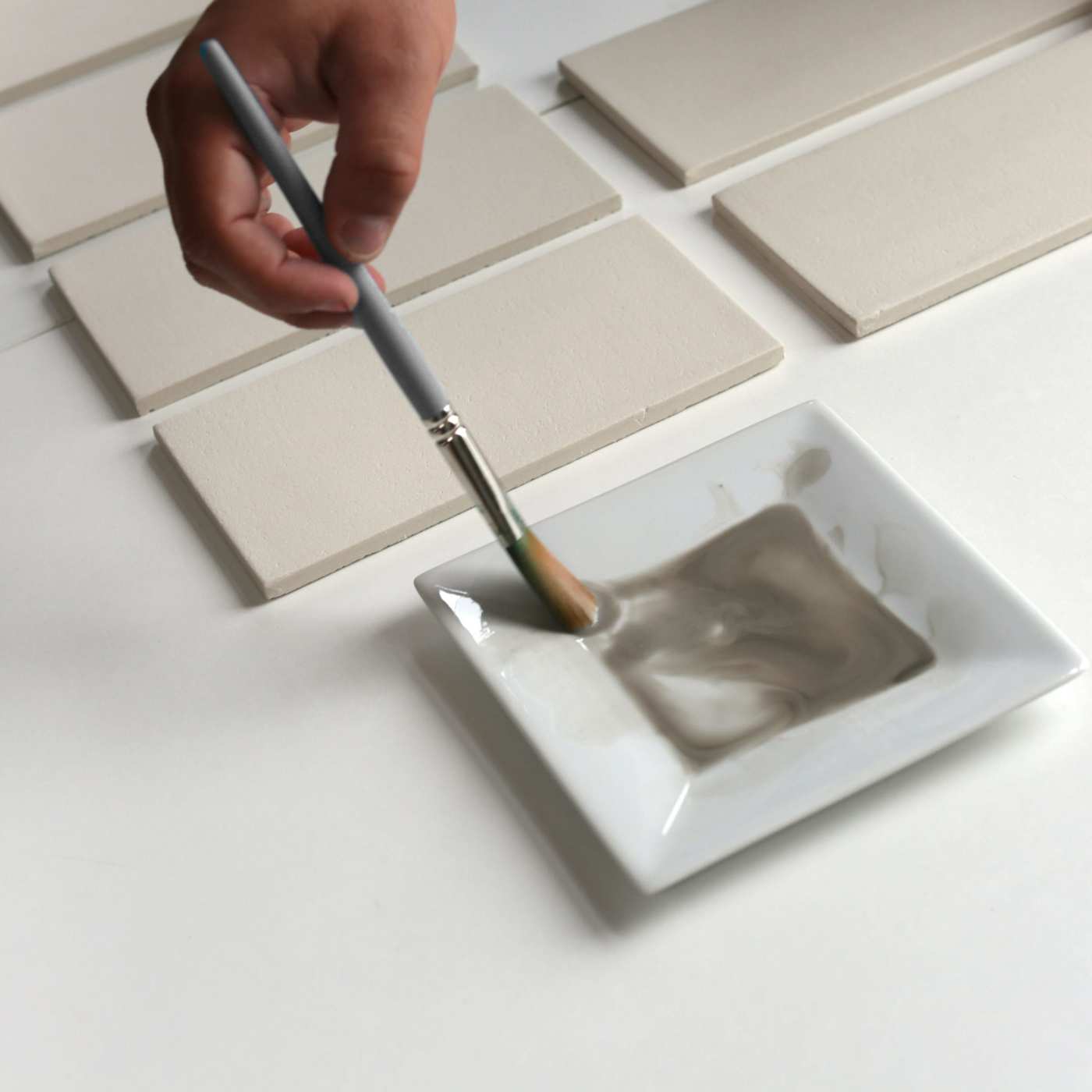 a person dipping a brush in paint to apply paint to blank tiles.