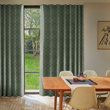 Panel curtains (green-and-cream checkerboard), floor-to-ceiling, mostly closed with a narrow central gap revealing a tall window and grassy yard; dining table with beige chairs and a teapot on a runner.