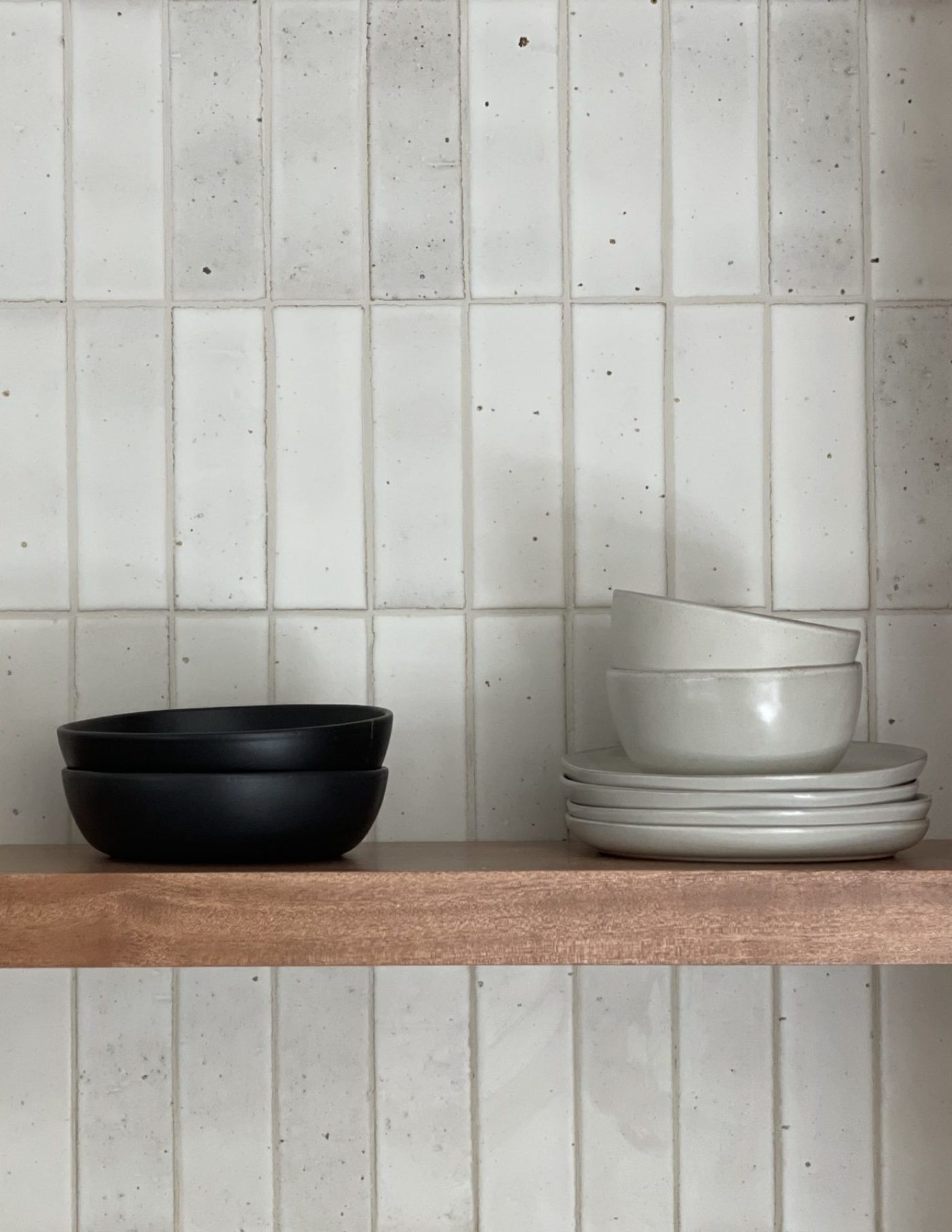 a white bowl sits on top of a wooden shelf in front of a white tiled wall.