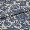Blue floral-and-grape patterned upholstery fabric, folded to show thickness and weave, printed in indigo on a natural beige ground; close-up, studio-lit textile surface.