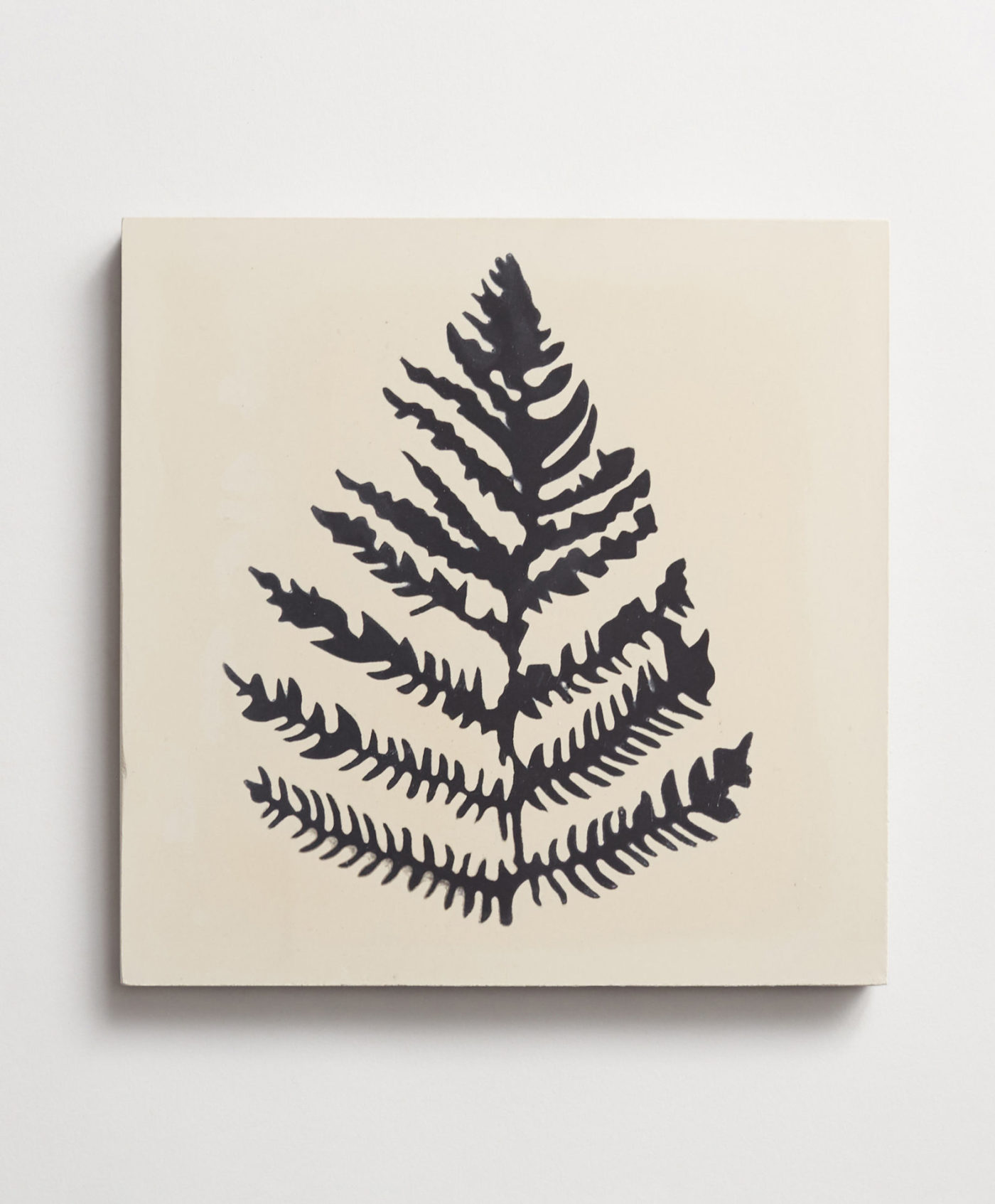 a tile with a black and white print of a fern leaf on a white background.