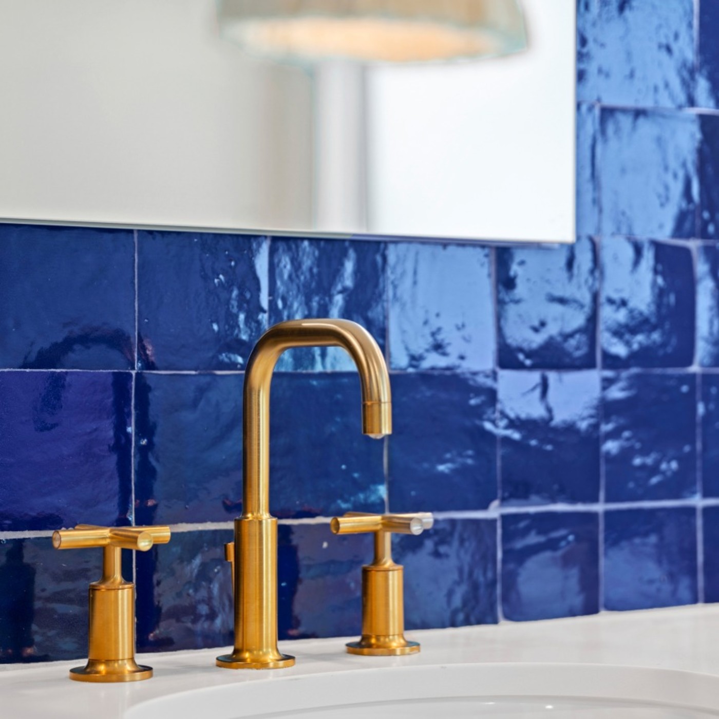 a blue tiledsink backsplash and a gold faucet.