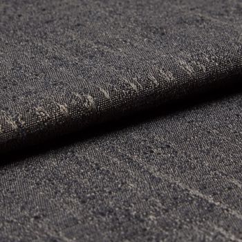 Dark gray woven fabric with slubs and subtle metallic threads; folded into a layered edge; tight macro close-up on a softly lit surface, neutral background suggesting an upholstery sample.