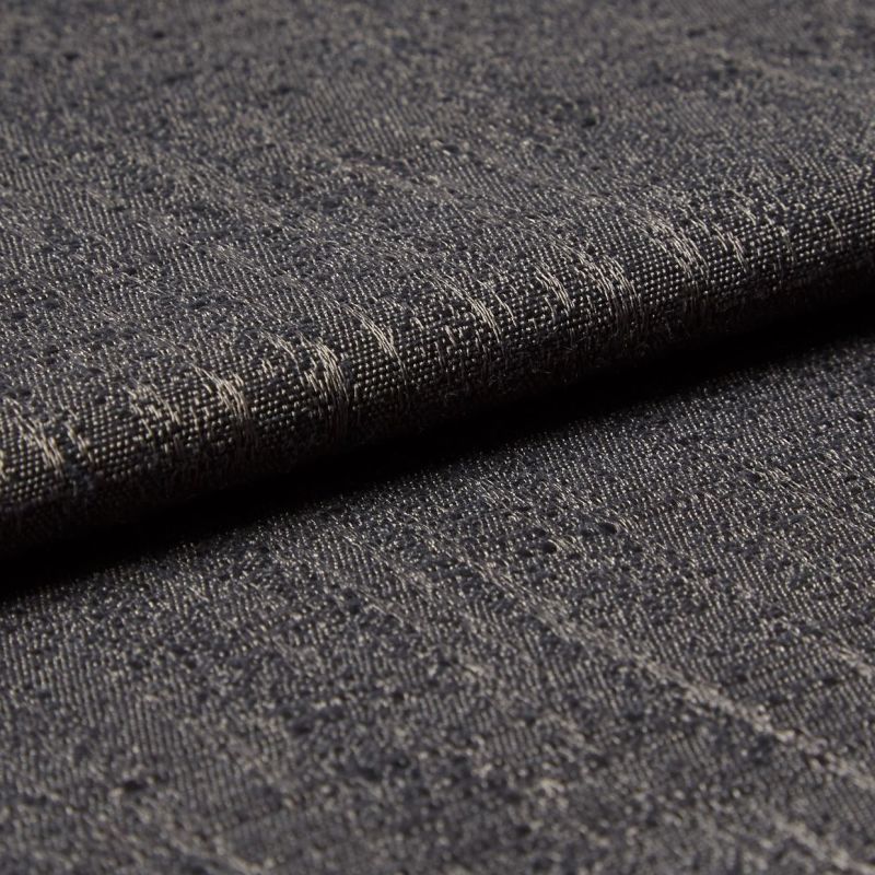 Dark gray woven fabric with slubs and subtle metallic threads; folded into a layered edge; tight macro close-up on a softly lit surface, neutral background suggesting an upholstery sample.