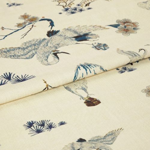 Light cream fabric with blue-grey crane and floral print, folded once; pattern visible across woven texture, photographed in soft studio light as a close-up product shot.