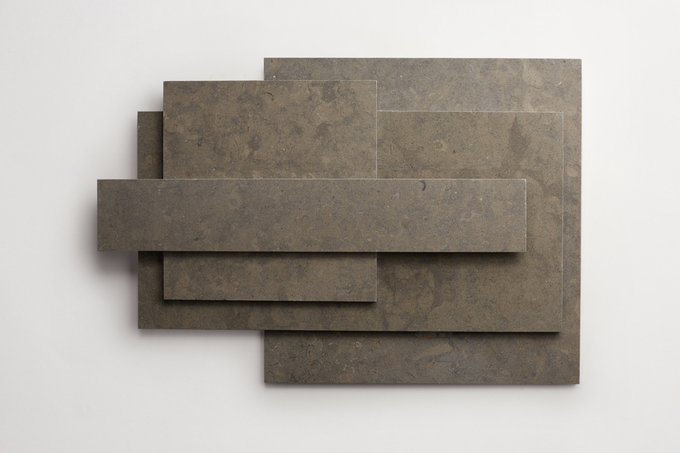 a stack of various sized grey limestone tiles on a white surface.