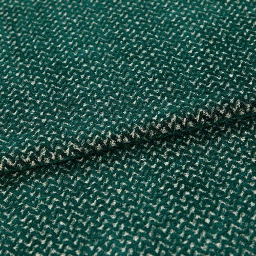 Green boucle-like fabric with dense cream zigzag pattern, folded into overlapping layers; close-up macro view on a neutral surface with soft, even lighting emphasizing the texture.