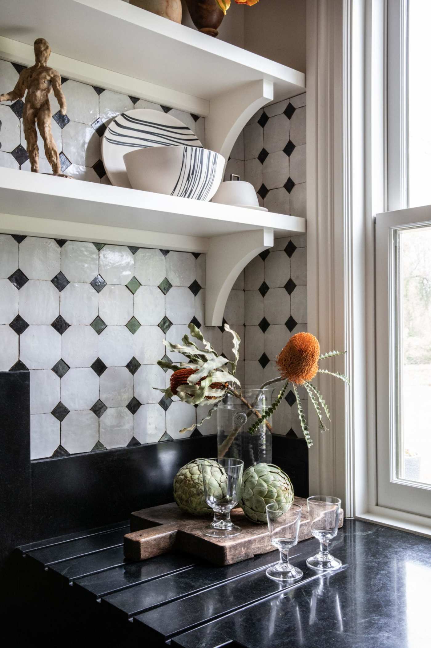 a kitchen corner with tiled wall and a vase and flowers.