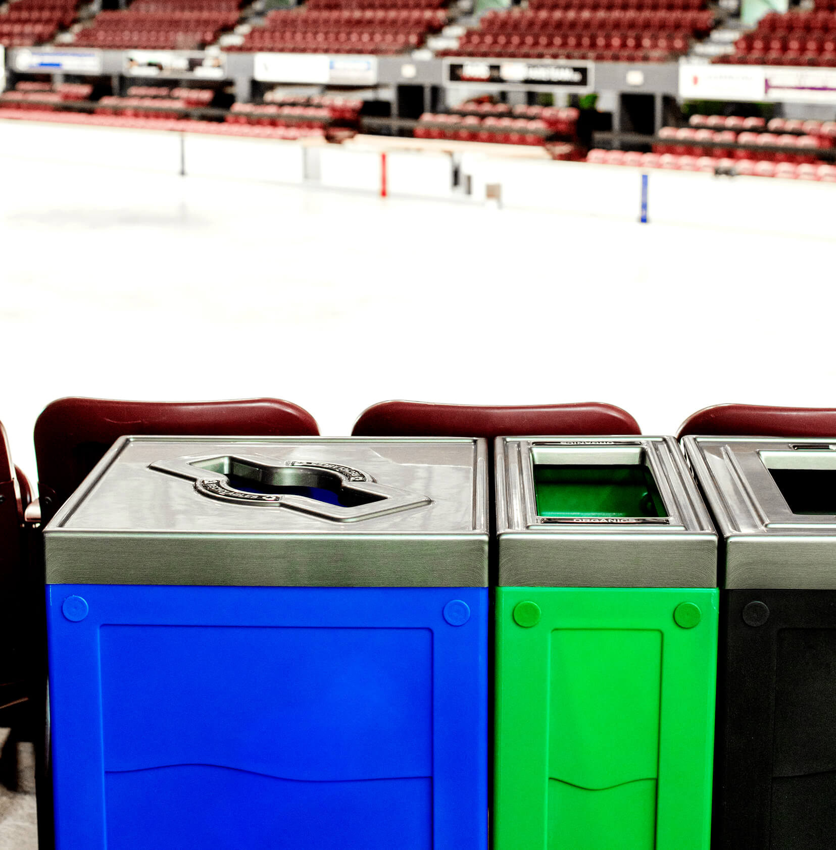 closeup of a recycling station with blue green and black bodies and pewter pattern lids at a hockey arena