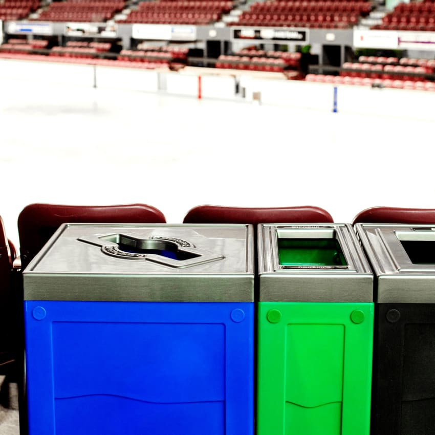 closeup of a recycling station with blue green and black bodies and pewter pattern lids at a hockey arena