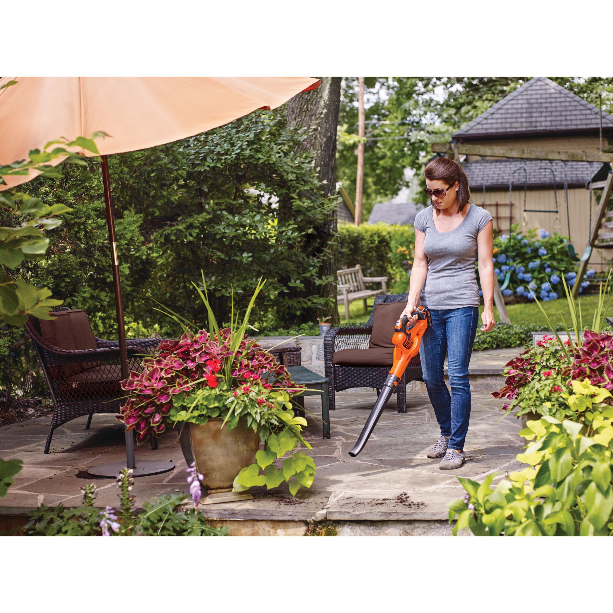 Woman using 20V Max Lithium Powerboost Sweeper on a patio with chairs and an umbrella.