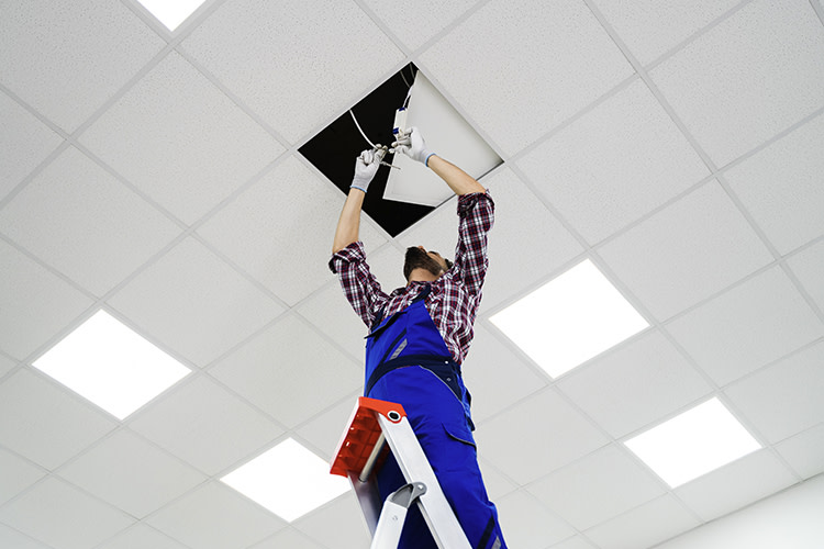 an electrician is on a ladder installing a light in a drop ceiling