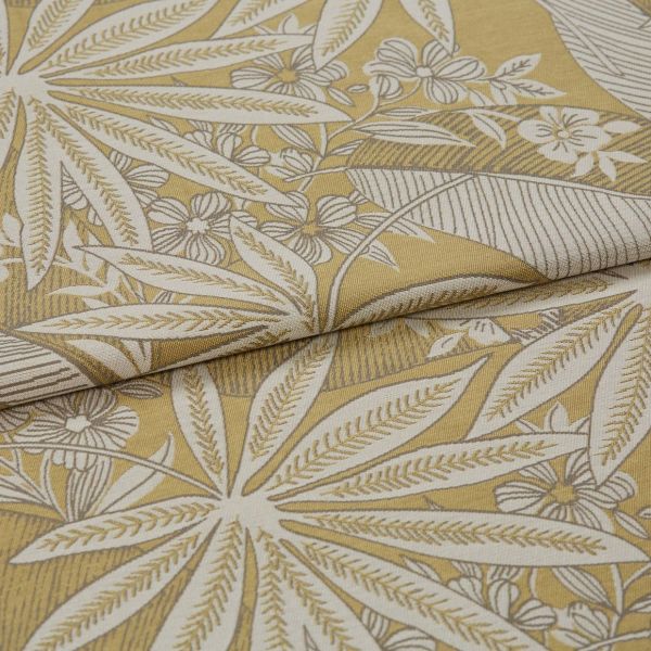 Botanical-patterned upholstery fabric, folded to show a layered edge; cream leaf-and-flower woven motif on mustard-yellow background, close-up studio shot with soft even lighting.