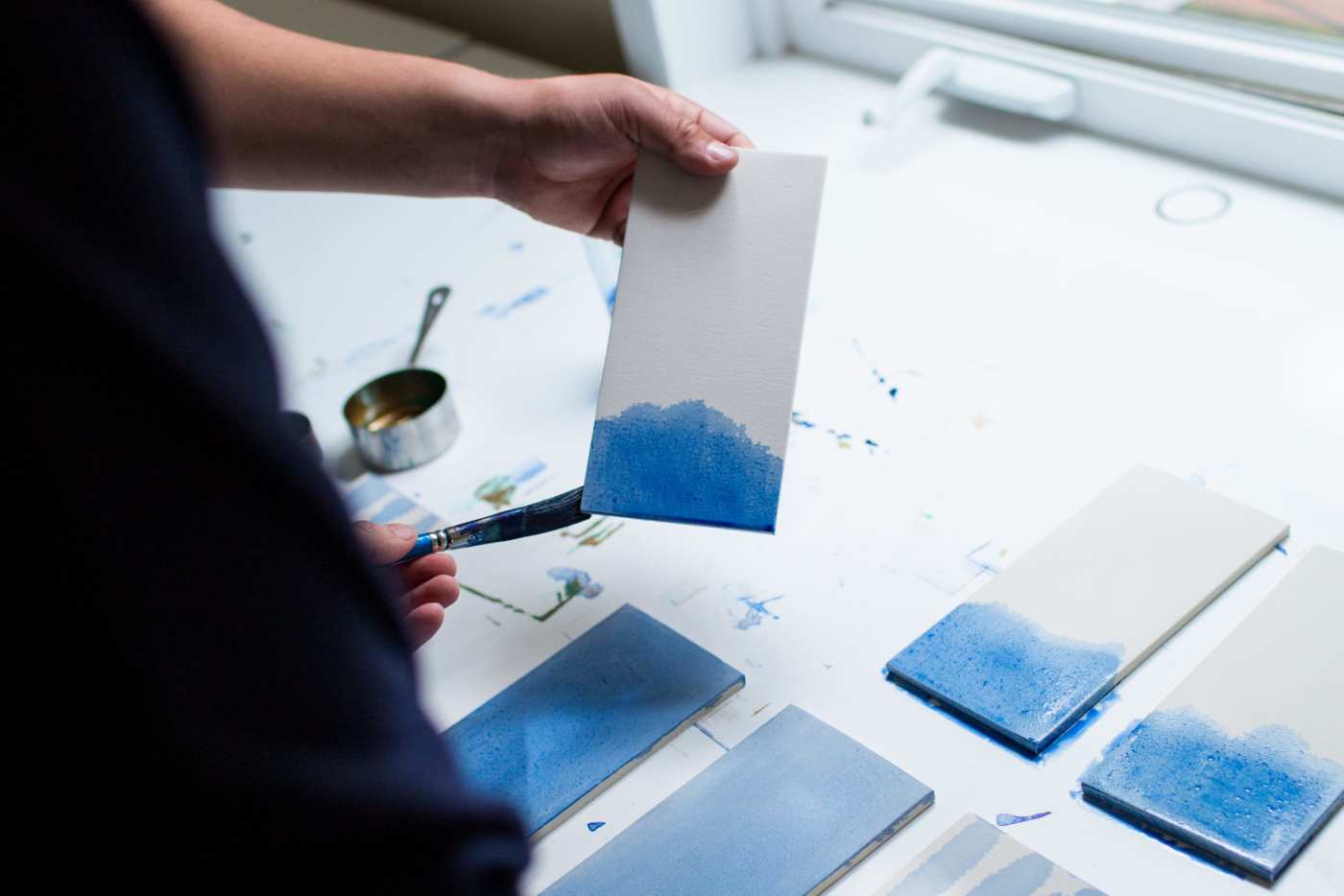 a person painting a piece of white tile with blue paint.