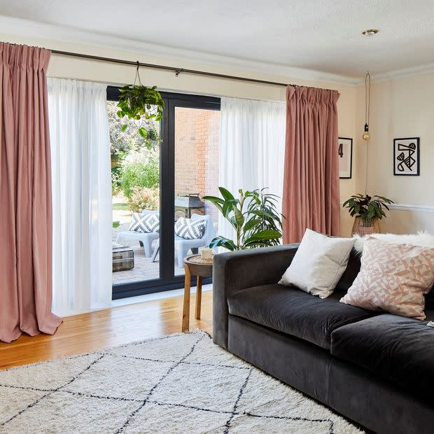 Floor-length blush-pink pleated curtains with sheer panels on a black rod, pulled to sides while sheers filter daylight; framing sliding glass doors to a sunny patio in a living room.