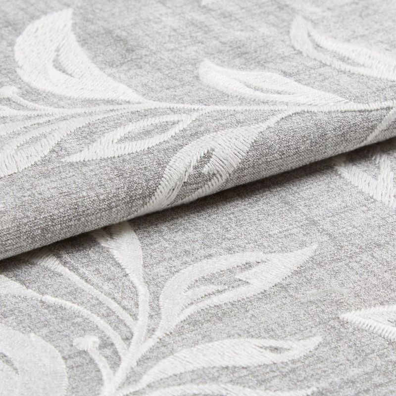 Textured gray fabric with raised white leaf embroidery folded and partially rolled, overlapping; close-up studio-lit view highlighting the weave and embossed botanical pattern.