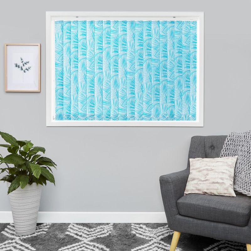 Blue palm-leaf patterned vertical blinds covering the window, fully closed and filtering daylight; in a gray-walled living room with a potted plant, framed print, gray armchair and patterned rug.