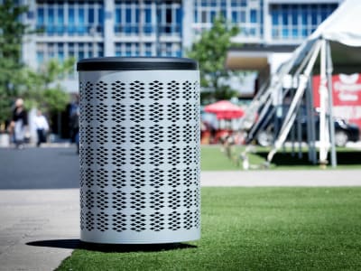 silver metal waste and recycling container with a plastic canopy lid sitting on the sidewalk in a busy city