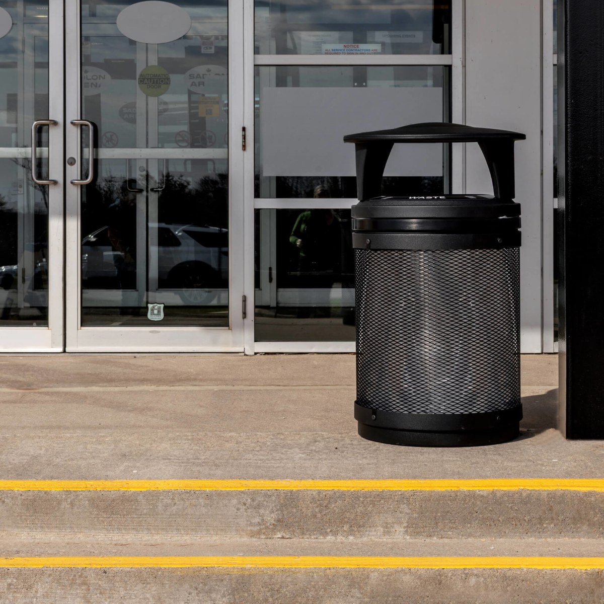 black metal and plastic waste bin with a canopy lid outdoors at a hockey arena