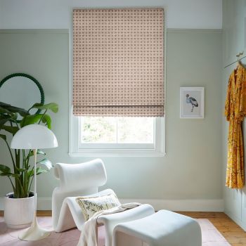 Patterned beige Roman blind lowered over central window, partially closed and softening daylight through a slim gap; in pastel-green reading nook with sculptural chair, plant, lamp, bird print and yellow robe.