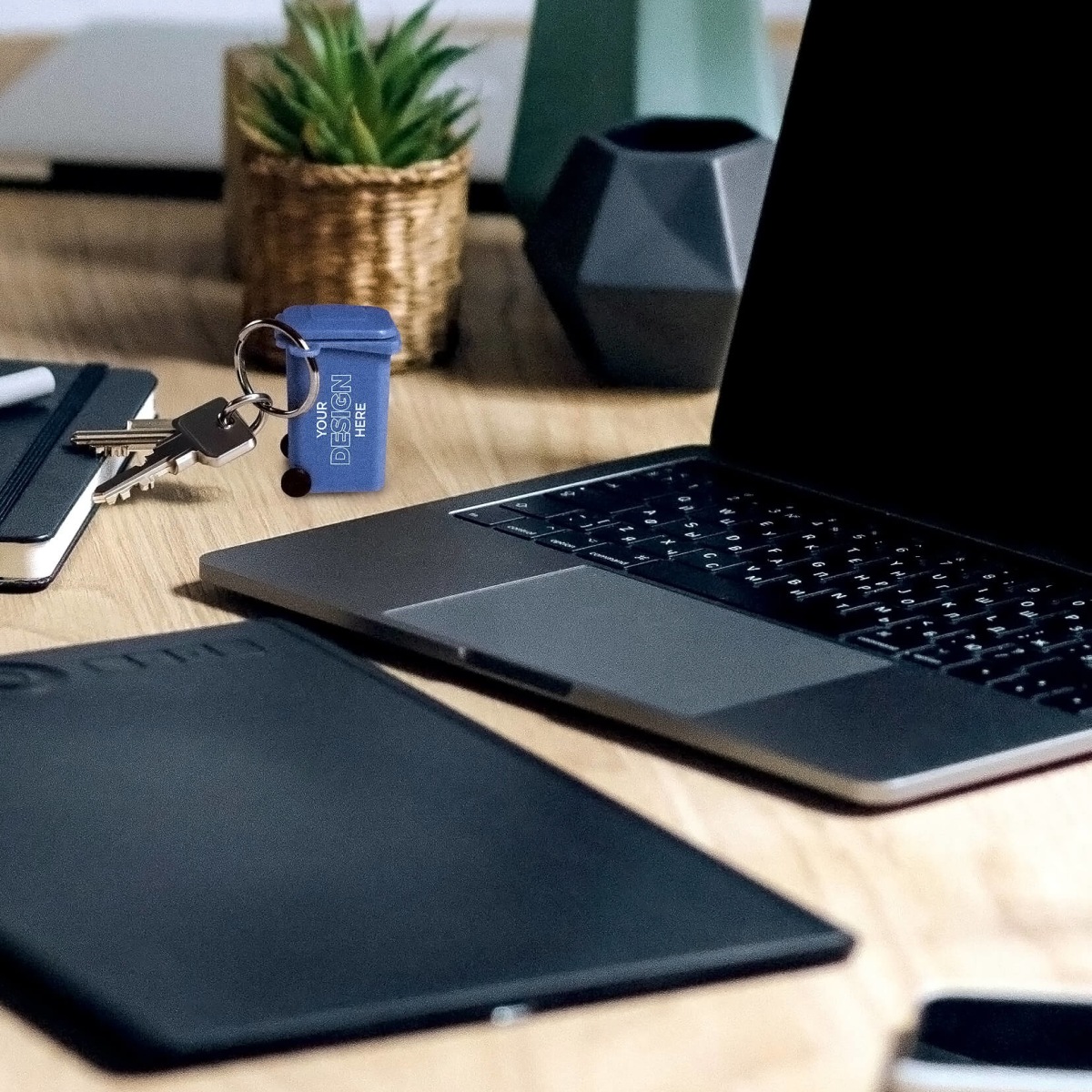 mini blue recycling cart keychain sitting on an office desk beside a laptop