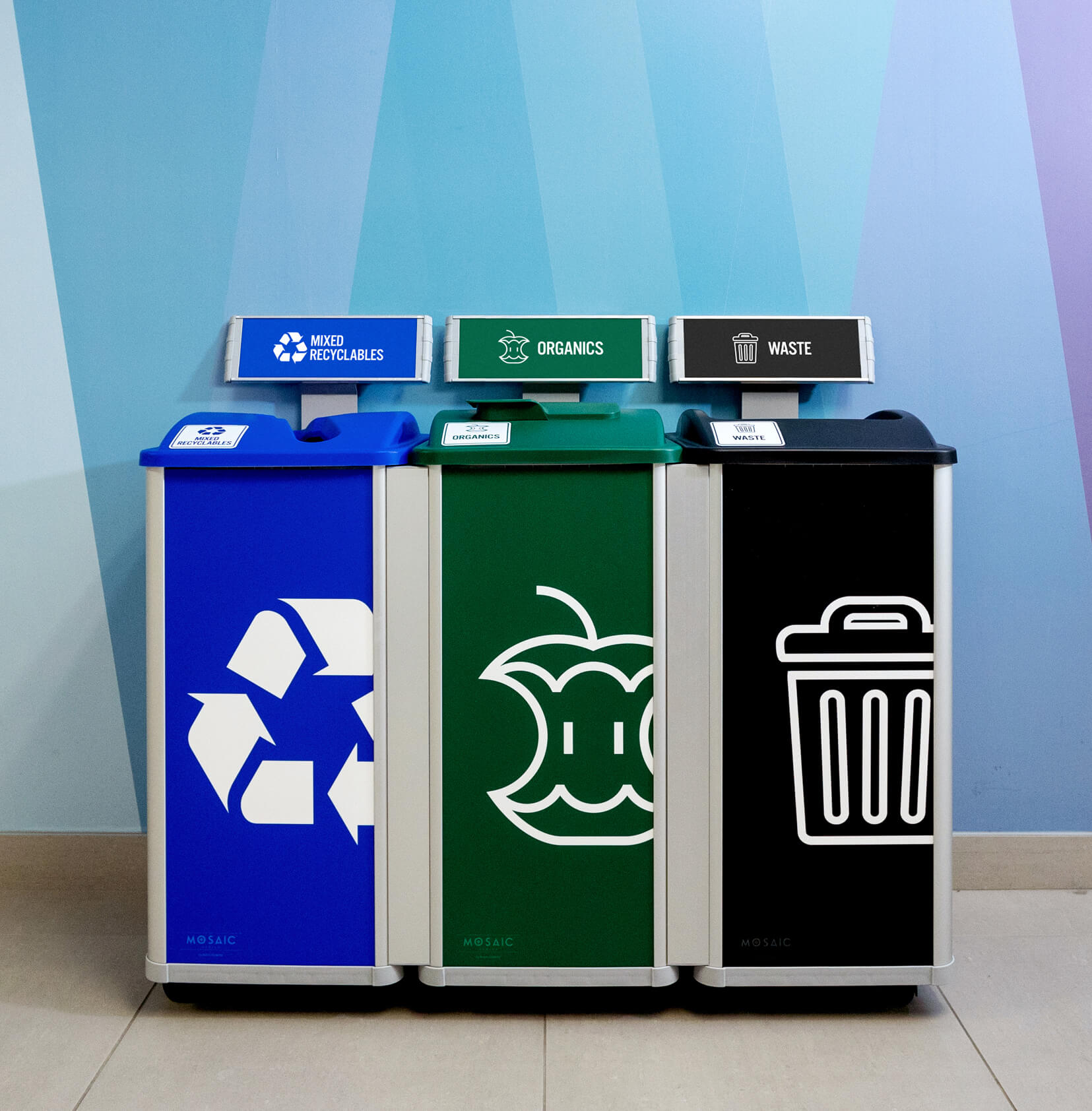 triple connected recycling organics and waste container system with body signs and sign frames in a brightly colored hallway at a college campus